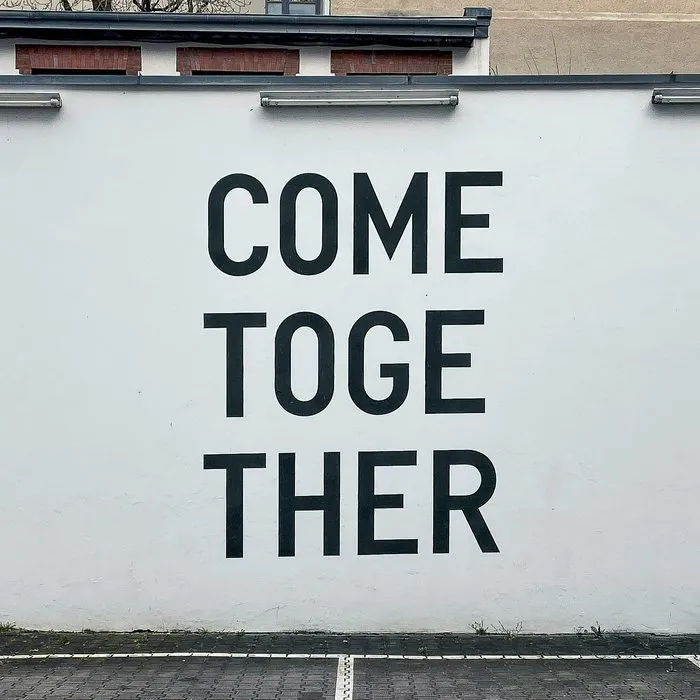 A white wall with the words Come together in large black letters